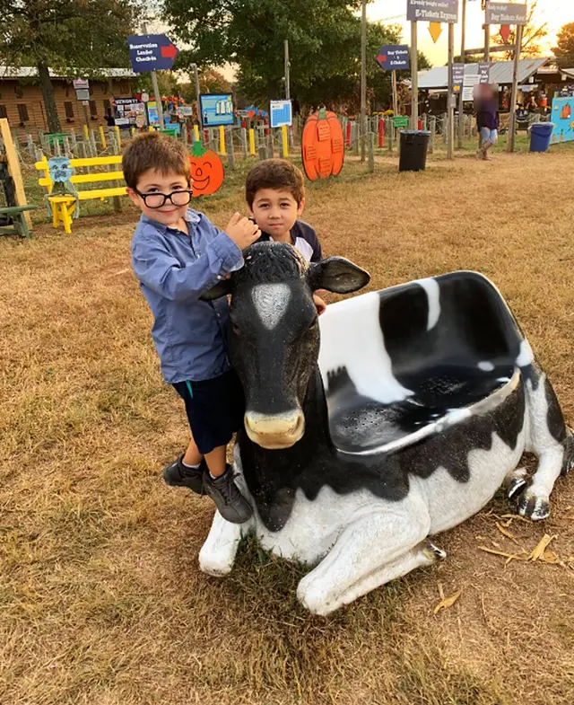 Two children from the Bereket Farmstead family posing with a black and white cow statue on a fall evening